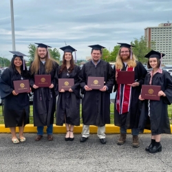 Students dressed in cap and gowns pose with degrees